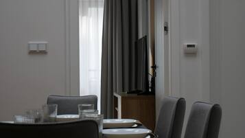 A modern dining area with a wooden table, grey upholstered chairs, and a television mounted on the wall.