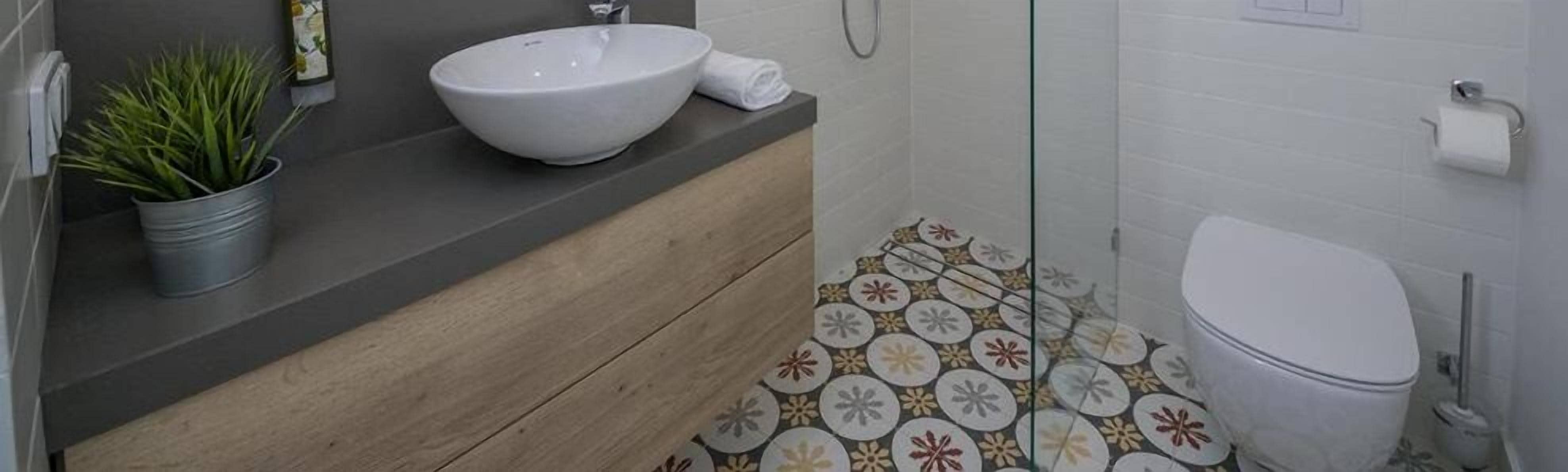 A bathroom with a wooden vanity, a white sink, a toilet, and a shower area.