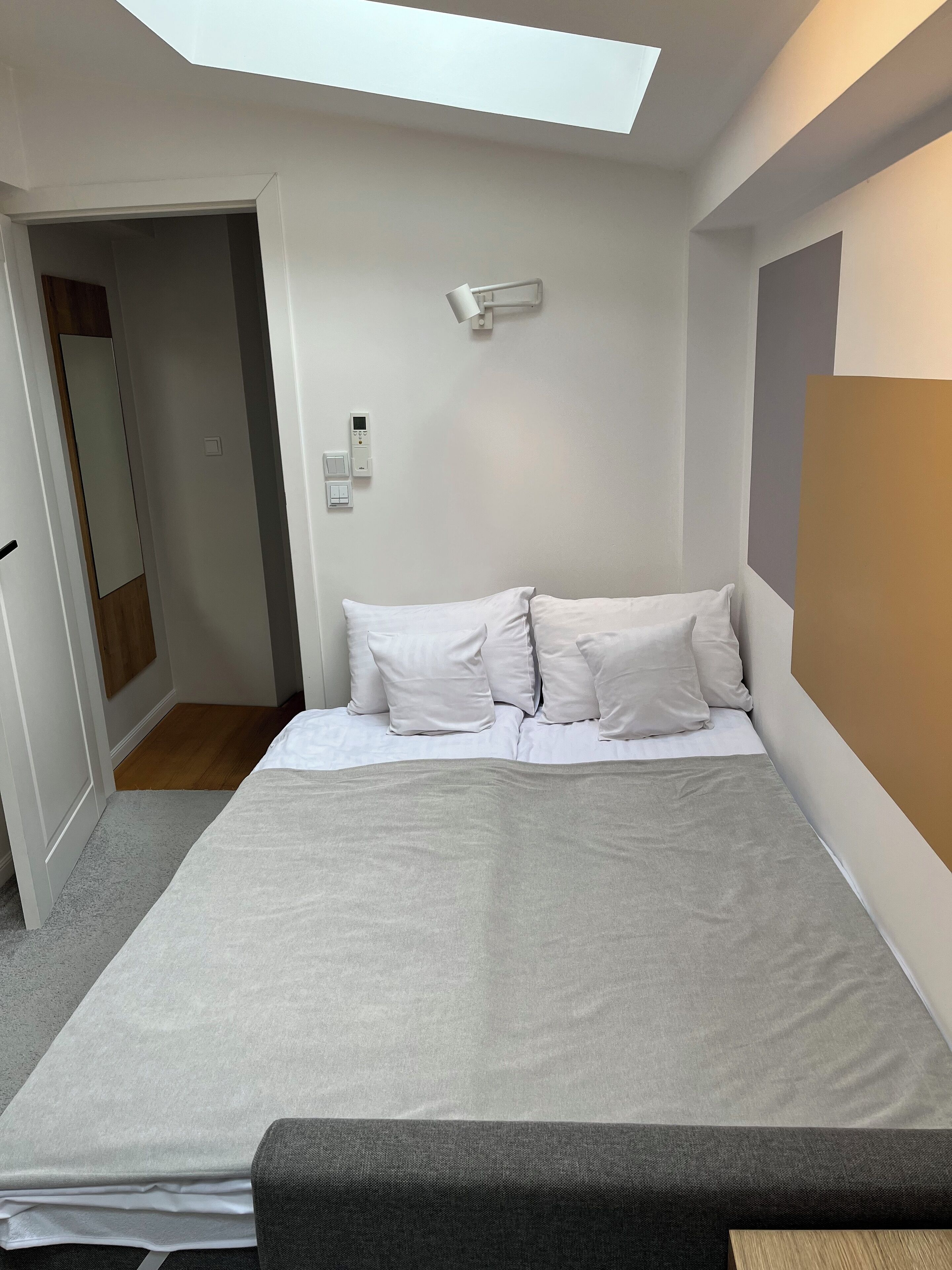 A bedroom with a bed, a bedside table, a ceiling light, and a door leading to another room.