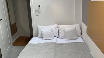 A bedroom with a bed, a bedside table, a ceiling light, and a door leading to another room.
