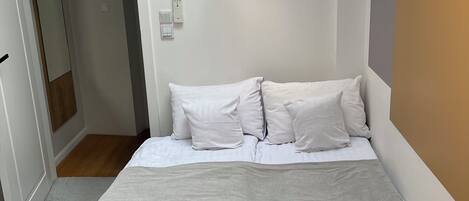 Un dormitorio con cama, mesita de noche, lámpara en el techo y puerta que da a otra habitación.