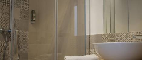 A bathroom with a glass shower enclosure, a large white sink, and a wooden vanity.