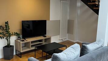 Una sala de estar moderna con un sofá gris, un televisor de pantalla plana sobre un soporte de madera, una mesa de centro negra y una planta en maceta.