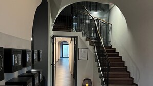 A hallway with a patterned floor, a staircase with a metal railing, and a chair. - Ermine Suites (Kraków)