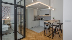 A modern kitchen with a dining area, featuring a wooden herringbone floor, a small kitchen island, and a bar stool seating arrangement. - Ermine Suites (Kraków)