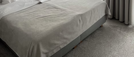 Un dormitorio moderno con una cama grande, un muro con diseño geométrico, una mesita de noche con lámpara y cortinas traslúcidas.