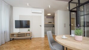 A modern living room with a flat-screen TV, a wooden dining table, and a gray chair. - Ermine Suites (Kraków)