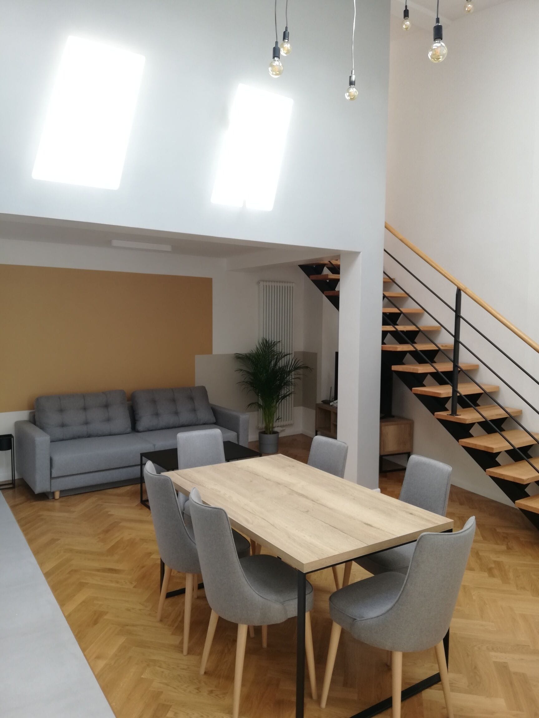 Un espace de vie moderne comprenant un coin repas, un canapé gris, un plancher en bois et un escalier.