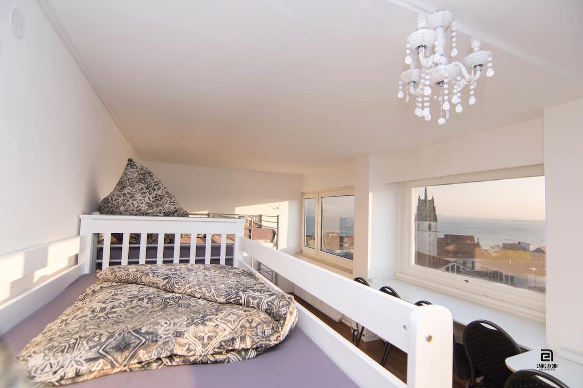 A bedroom with a bed, a window with a view, a chandelier, and a balcony.