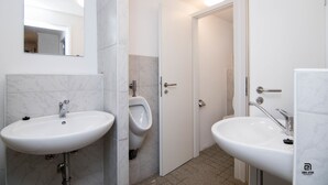 A modern bathroom with two white sinks, a urinal, and a door leading to another room. - Skyhostel Friedrichshafen (Friedrichshafen)