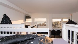 A room with bunk beds, a desk, two chairs, a window with a view, and a radiator. - Skyhostel Friedrichshafen (Friedrichshafen)