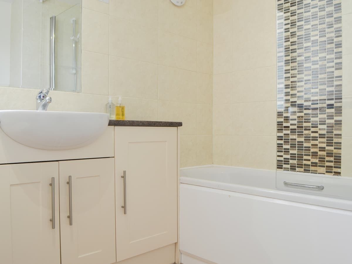 A bathroom with a white sink, beige cabinets, and a bathtub.