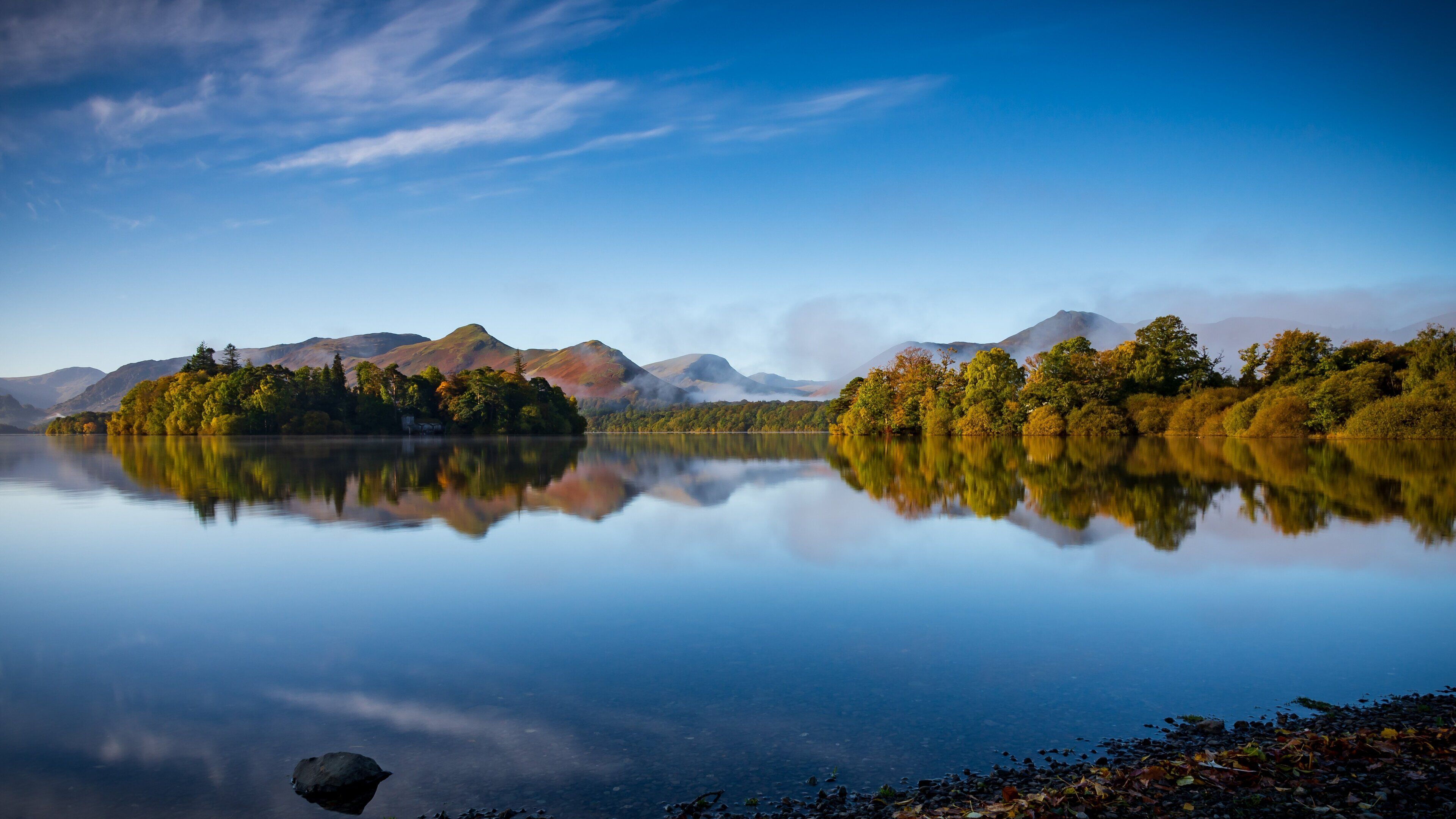 A calm lake with a clear reflection of the surrounding trees and mountains.