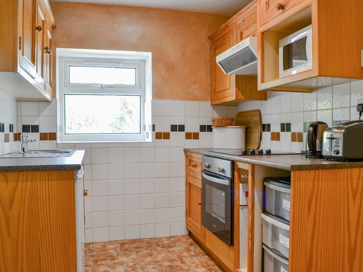 A compact kitchen with wooden cabinets, a built-in microwave, a toaster, and a window providing natural light.