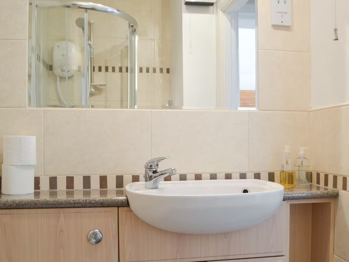 Un baño con lavamanos blanco, espejo y cabina de ducha.