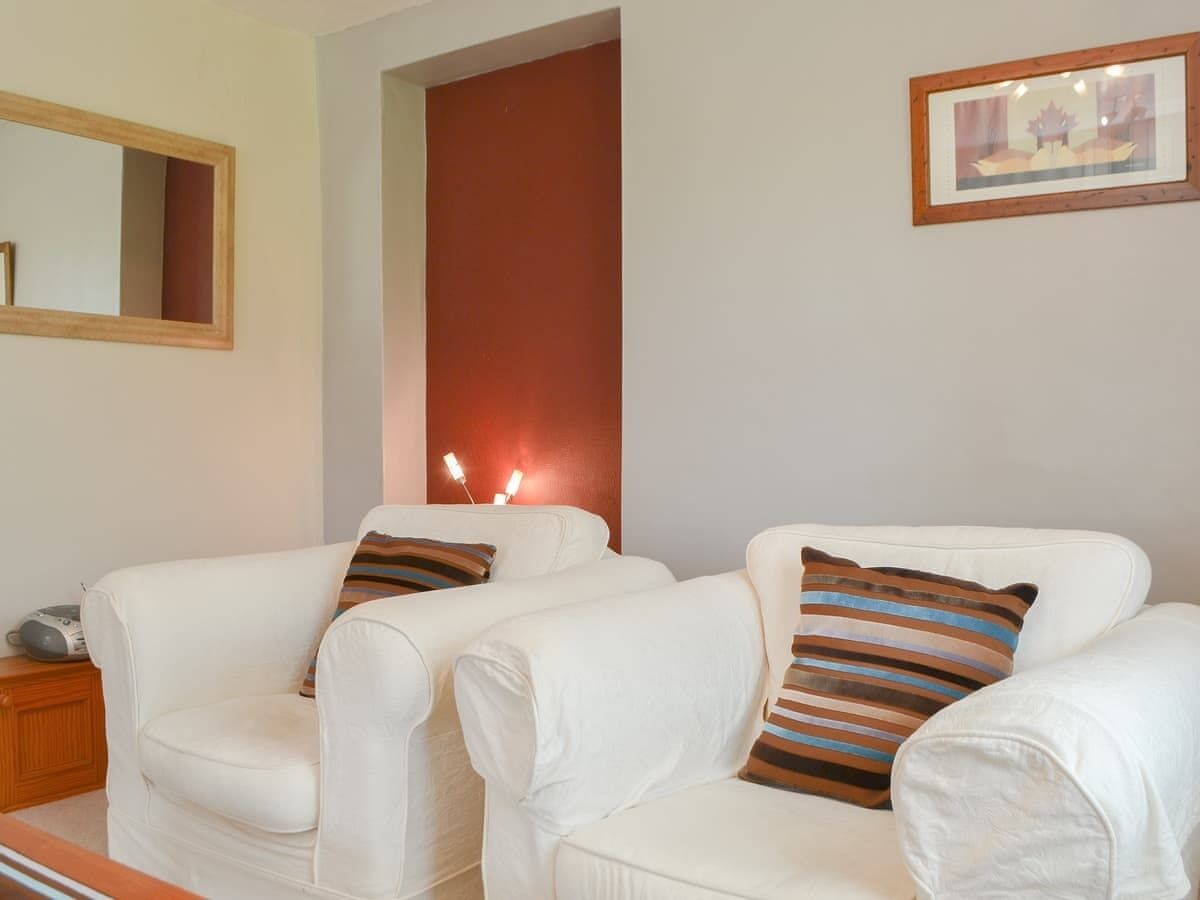 Un soggiorno con due poltrone in pelle bianca, un tavolino in legno con una radio e un quadro appeso al muro.