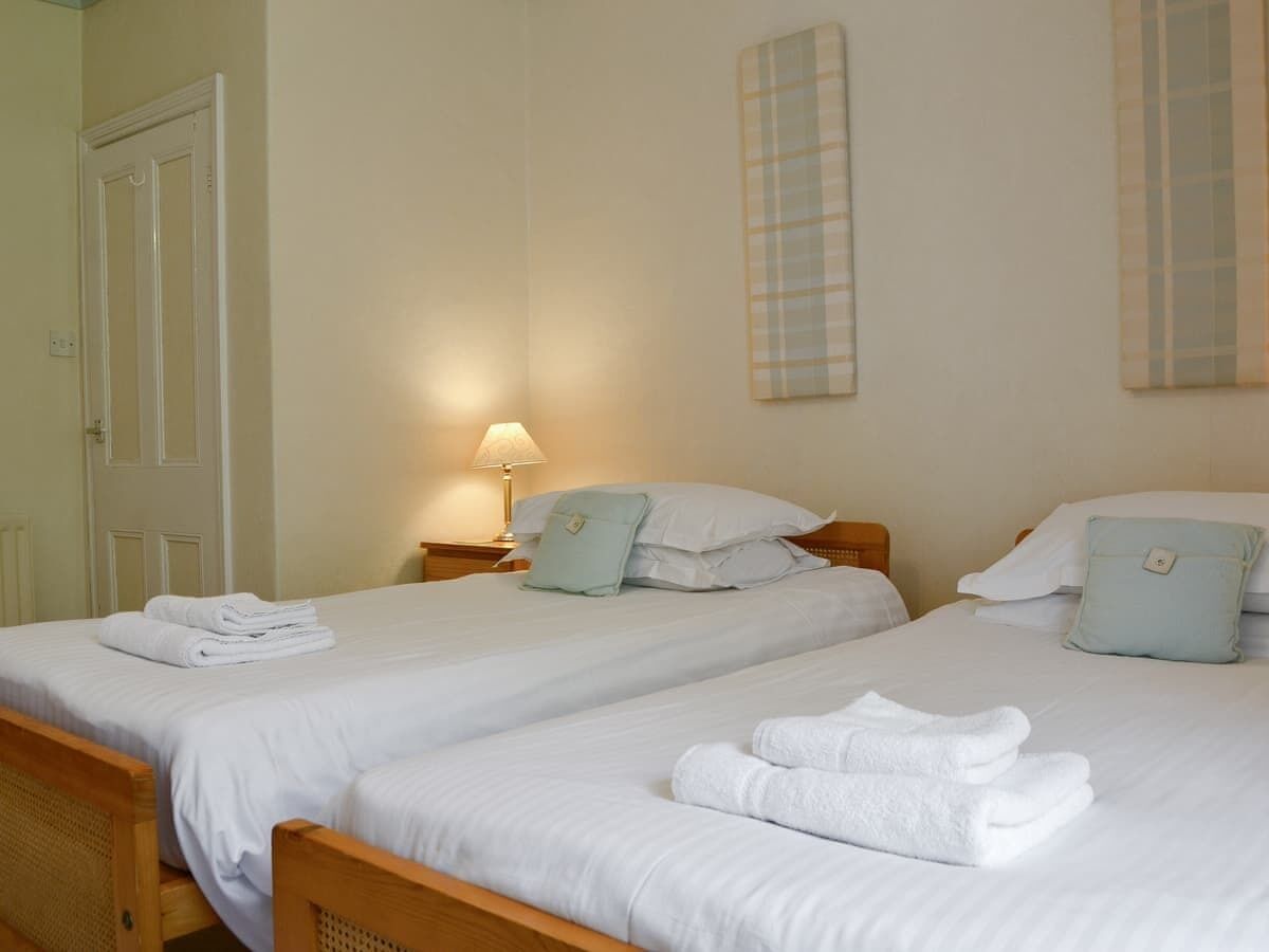 Een hotelkamer met twee enkele bedden, elk met keurig opgevouwen witte handdoeken. Daartussen staat een nachtkastje met een lamp, en links is een deur te zien.