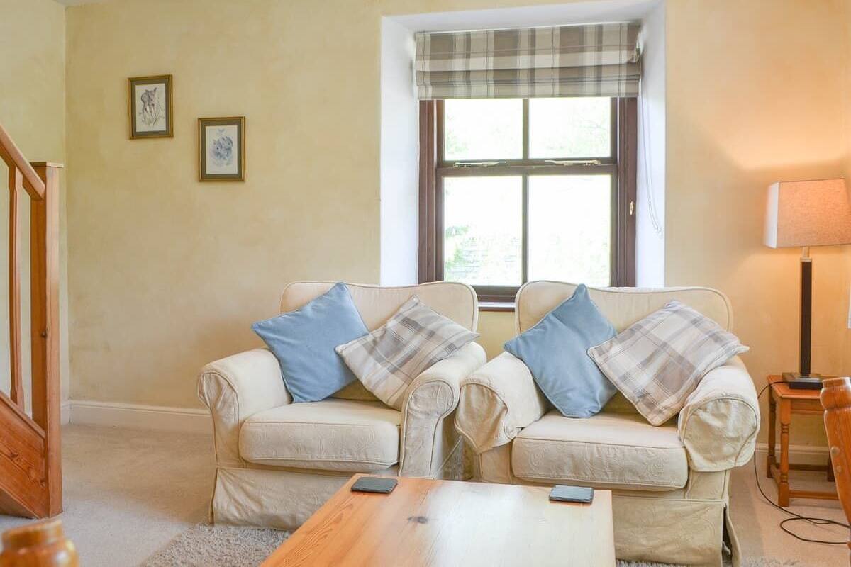 A living room with two cream-colored sofas, a wooden coffee table, a plaid window valance, and a lamp on a side table.