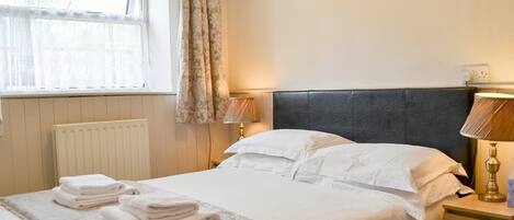 A neatly made bed with white linens and a patterned throw, a bedside lamp, and a window with curtains.