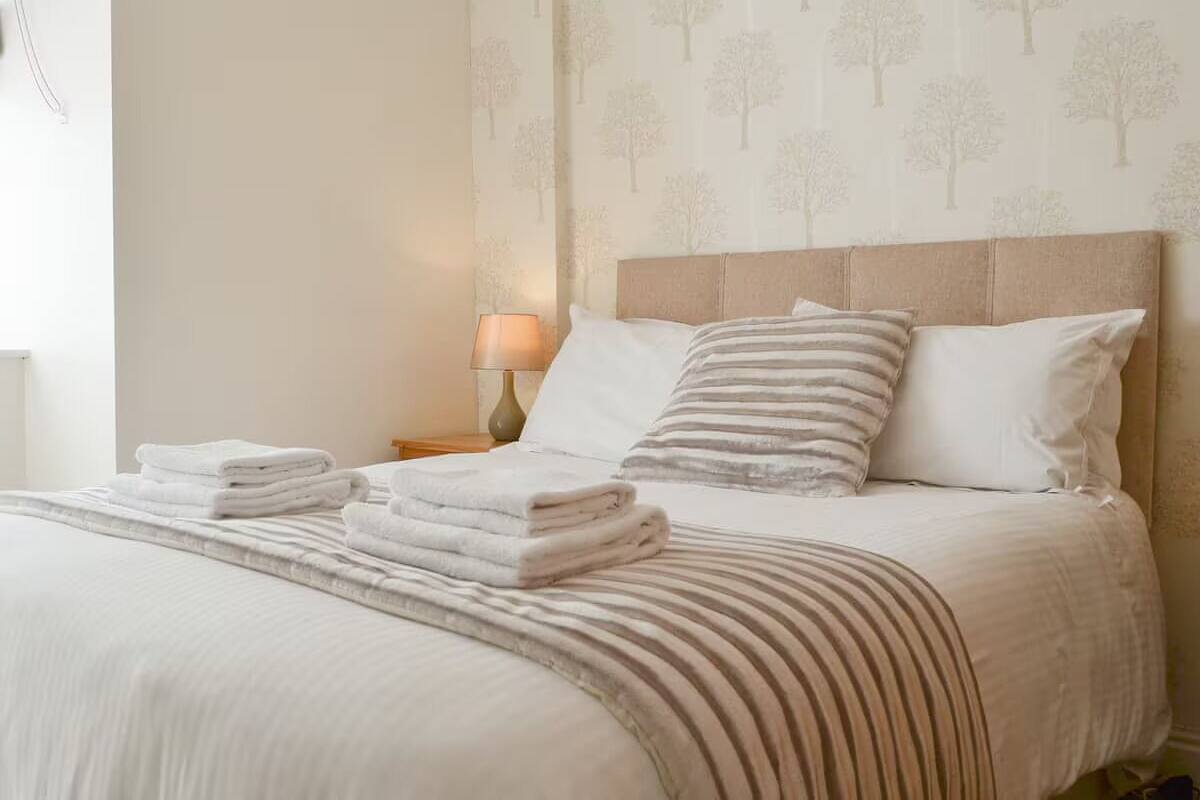 A neatly made bed with folded towels, a striped blanket, and a headboard with patterned wallpaper.