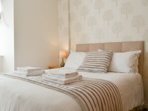 A neatly made bed with folded towels, a striped blanket, and a headboard with patterned wallpaper. - Brigham Farm Apartments (Keswick)