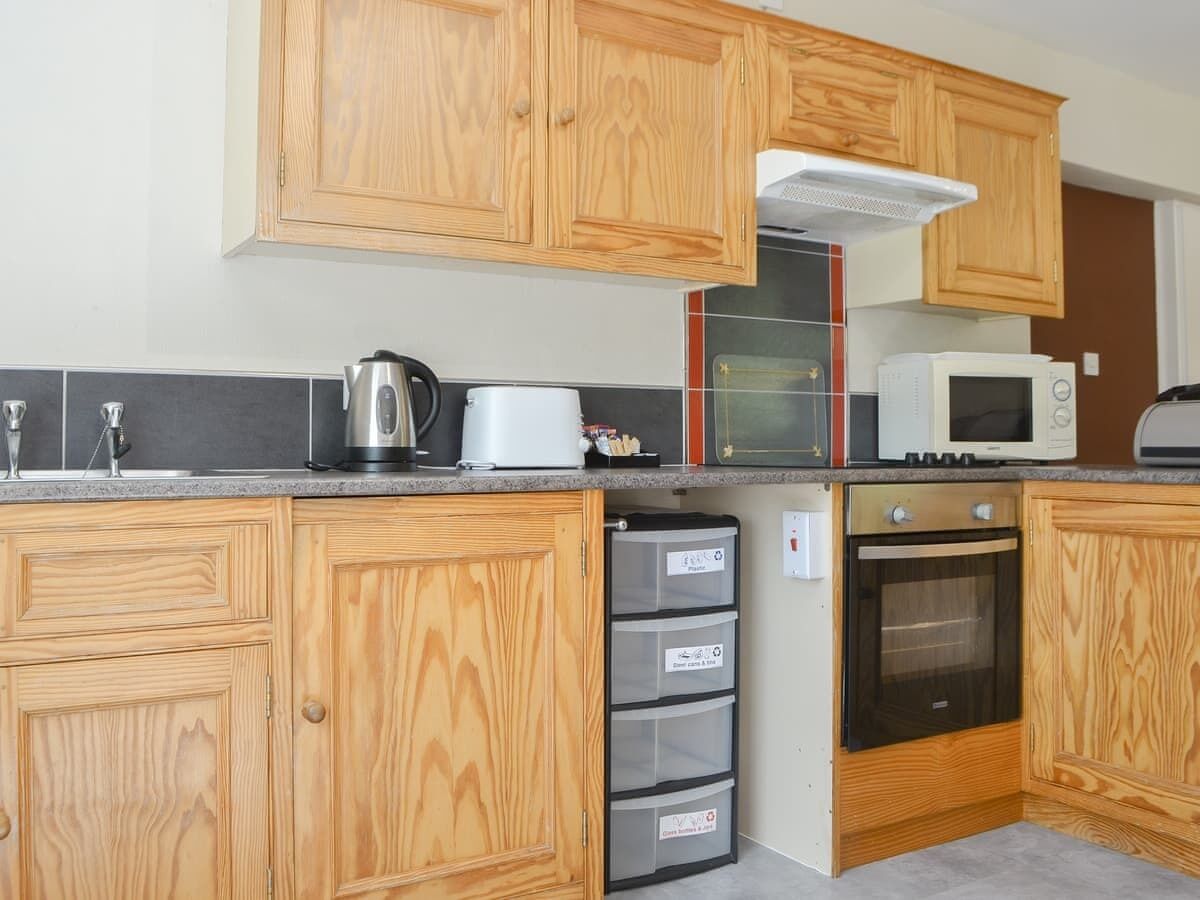 Una cocina compacta con armarios de madera, microondas, hervidor y horno empotrado.