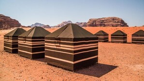 A row of striped tents in a desert landscape with rocky formations in the background. - Bedouin Nomads Adventures (Wadi Rum)