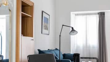 Une chambre d’hôtel moderne avec une armoire en bois, un bureau avec une lampe, un canapé bleu et une grande fenêtre avec des rideaux.