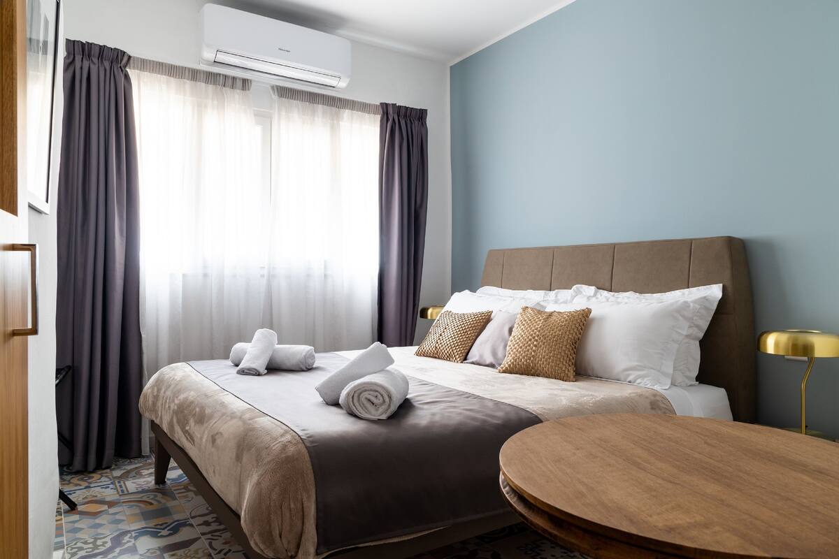 Ein Hotelzimmer mit Bett, Nachttisch, Lampe und einem Fenster mit Vorhängen.