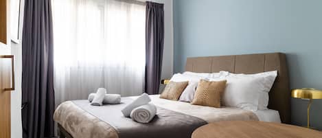 A hotel room with a bed, a bedside table, a lamp, and a window with curtains.