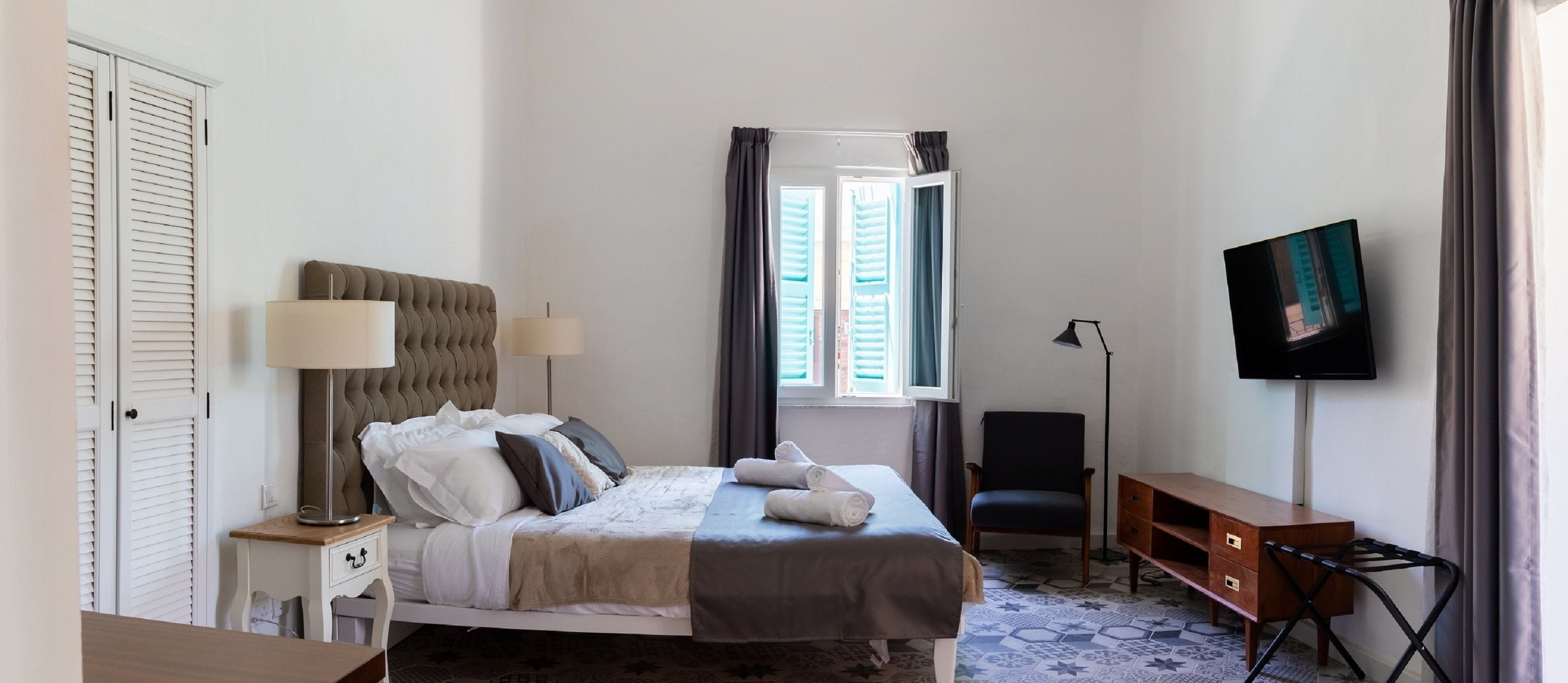 A neatly arranged bedroom with a bed, bedside lamps, a desk, a chair, and a TV.