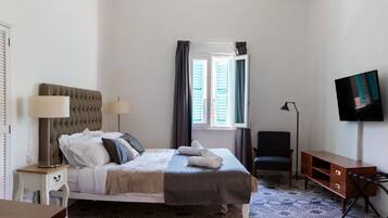 A neatly arranged bedroom with a bed, bedside lamps, a desk, a chair, and a TV.