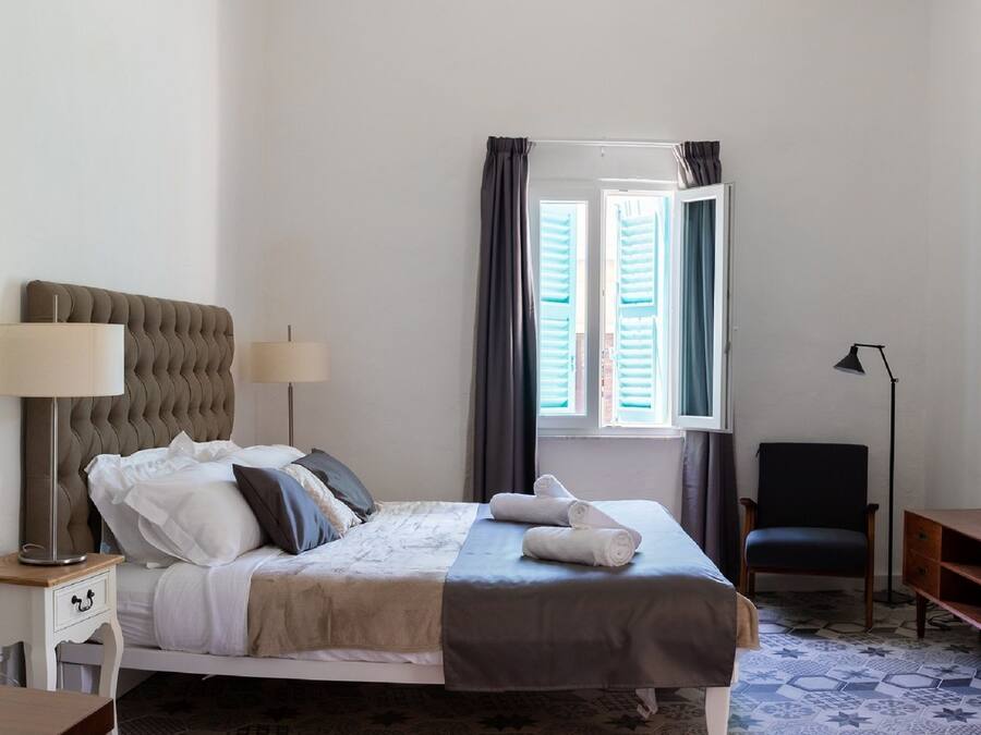 A neatly arranged bedroom with a bed, bedside lamps, a desk, a chair, and a TV.