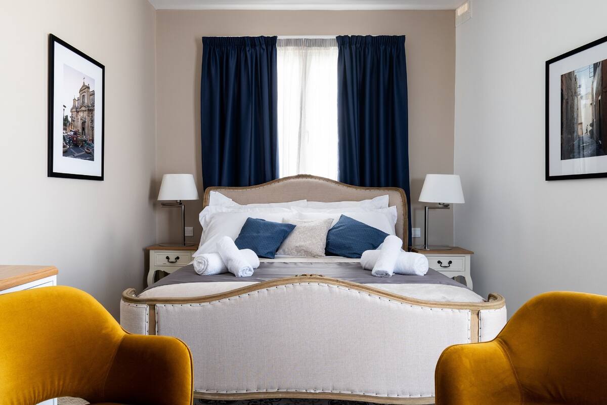 Ein ordentlich eingerichtetes Hotelzimmer mit Bett, zwei Nachttischen, einer Lampe und einem Sessel.