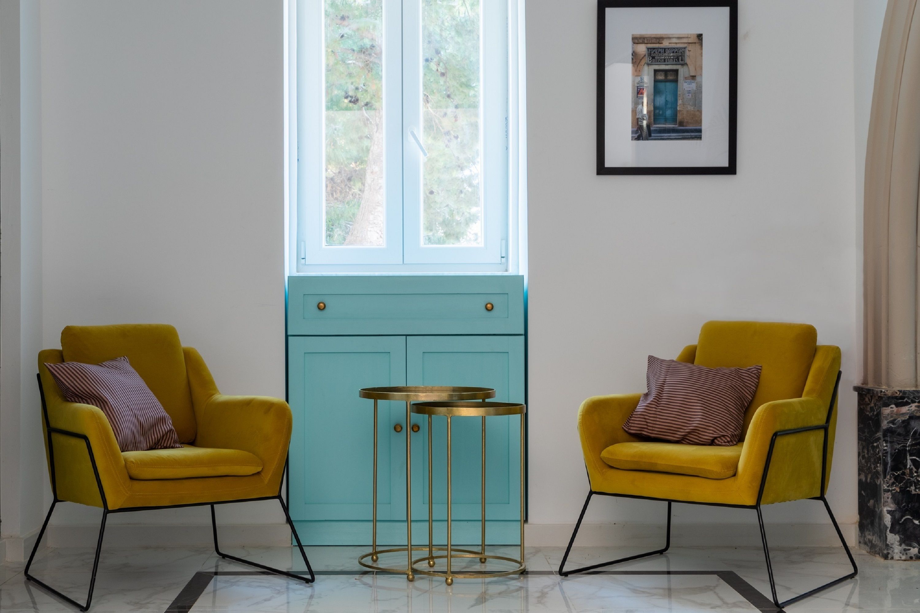 Une pièce avec deux fauteuils jaunes, une commode turquoise et une petite table ronde.