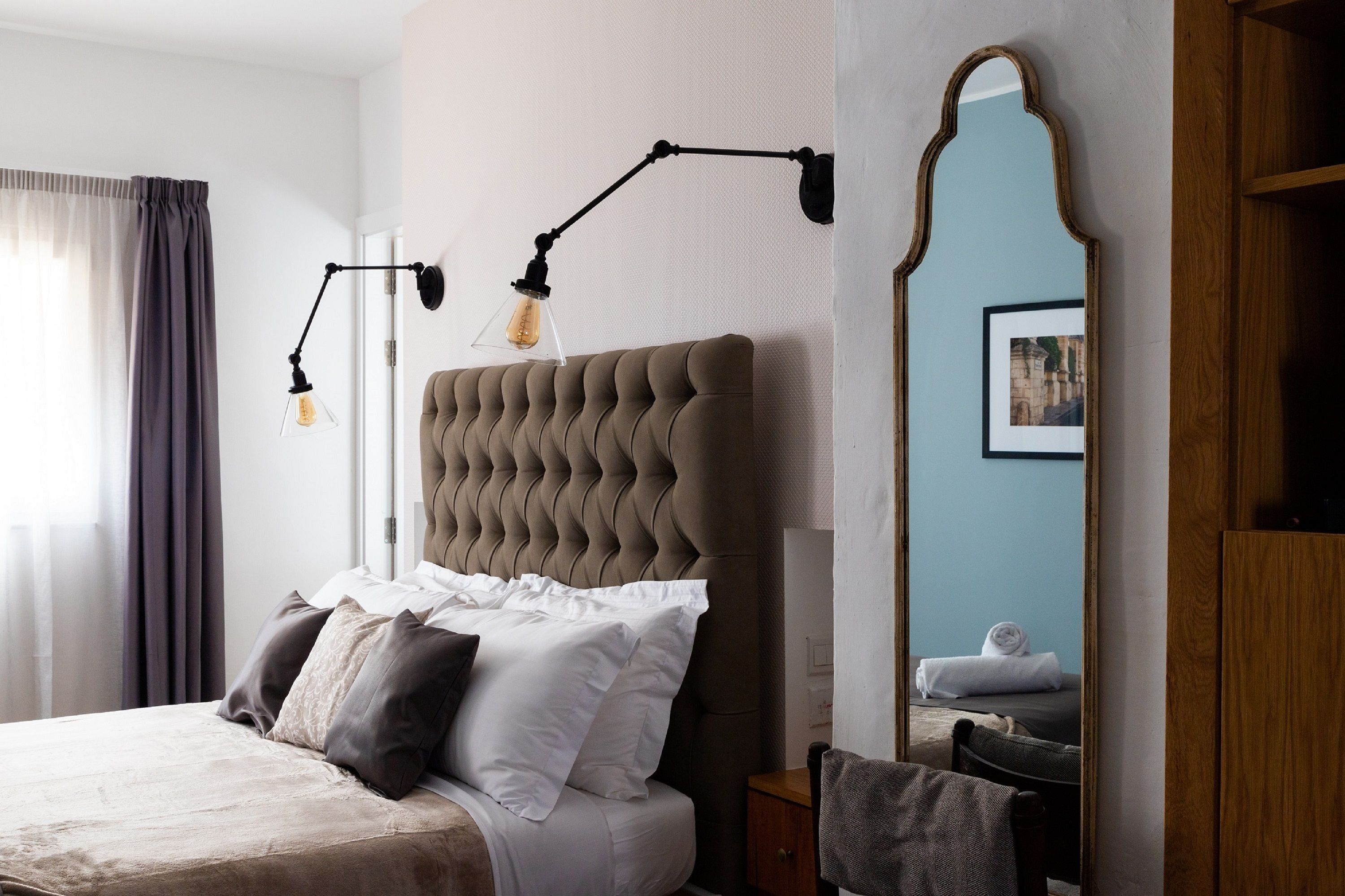 A neatly made bed with white and dark pillows, a tufted headboard, and a bedside table with a lamp.