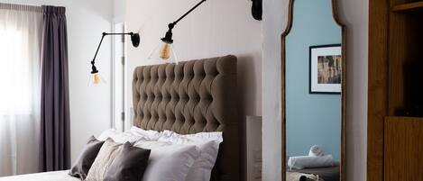 A neatly made bed with white and dark pillows, a tufted headboard, and a bedside table with a lamp.