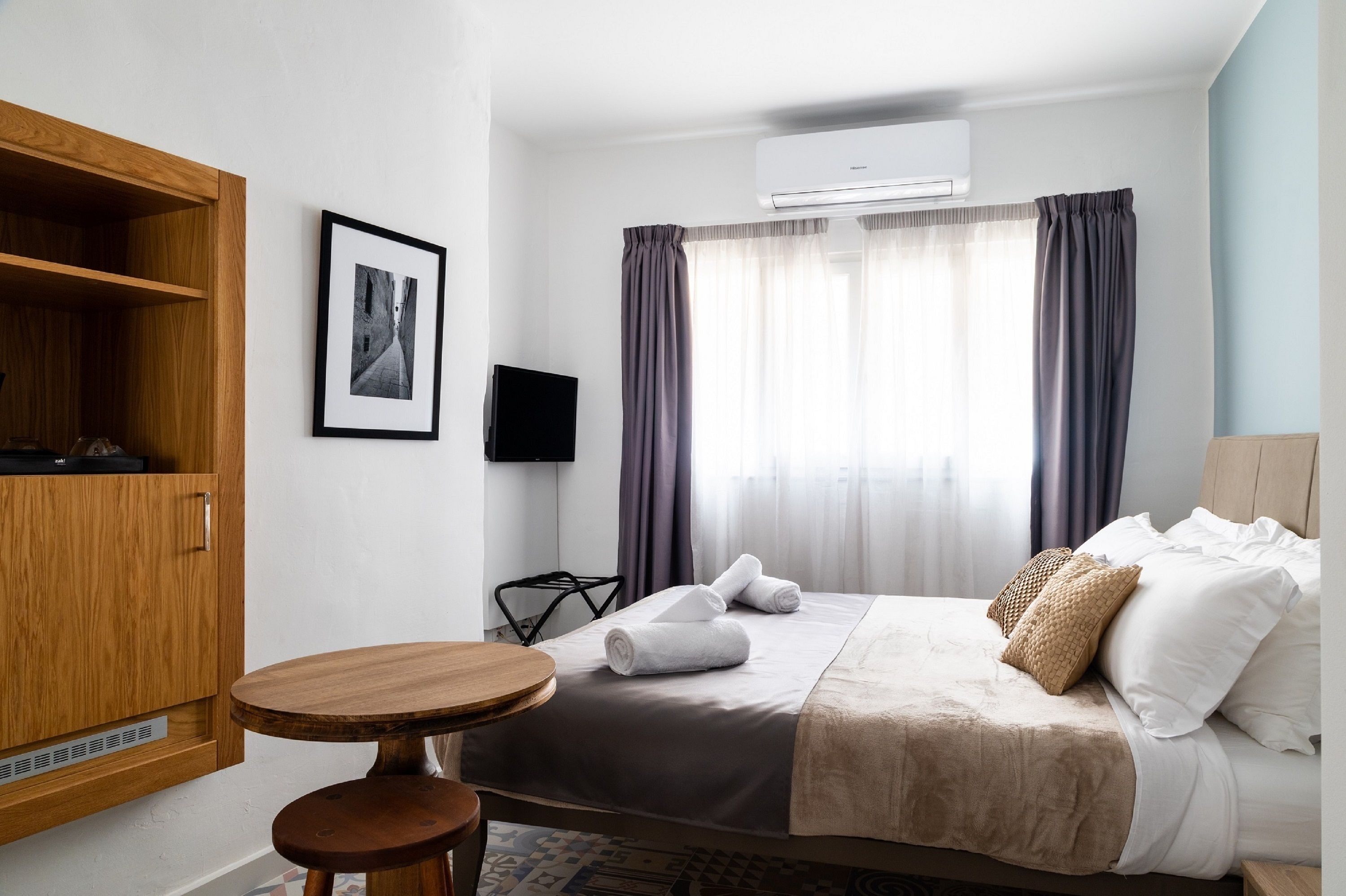 Habitación de hotel con cama, armario de madera, una mesita redonda, televisor y ventana con cortinas.