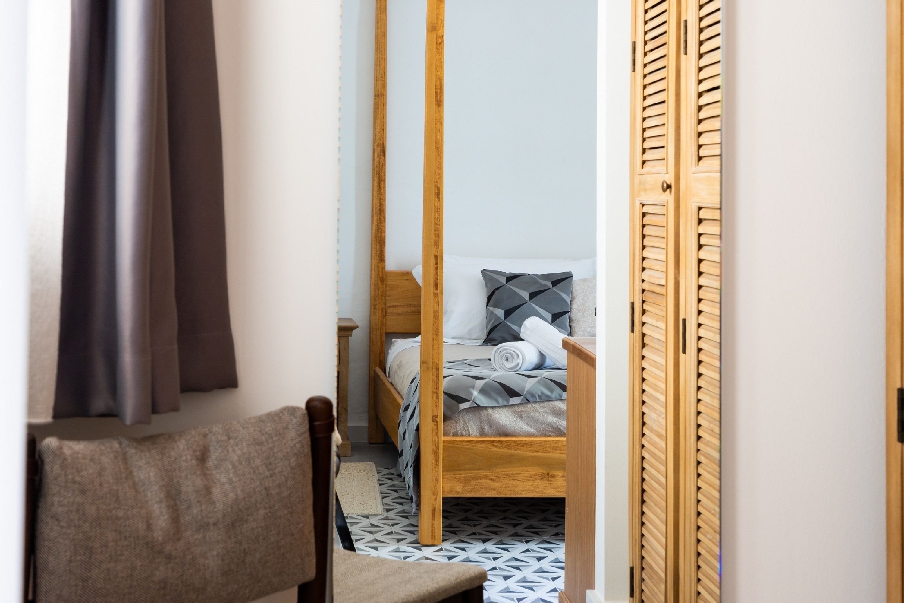 Een kleine kamer met een houten bed, een stoel en een garderobe.