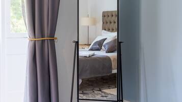 A room with a bed, a standing mirror, and a small table.