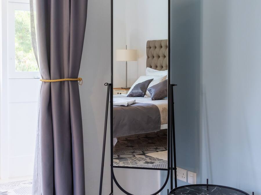 A room with a bed, a standing mirror, and a small table.