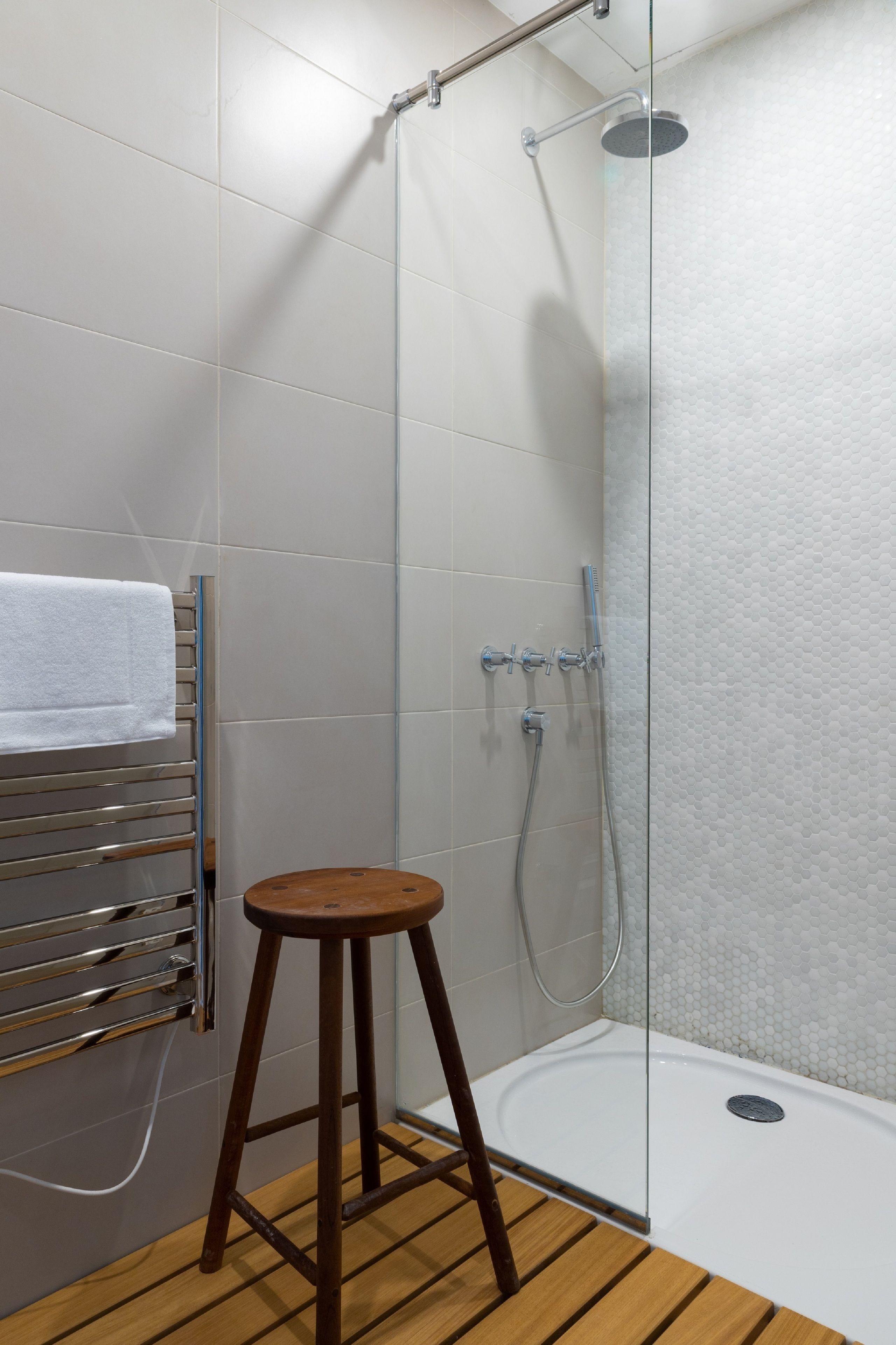 A shower area with a glass door, a wooden stool, and a towel rack.
