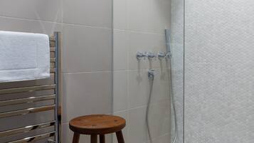 A shower area with a glass door, a wooden stool, and a towel rack.