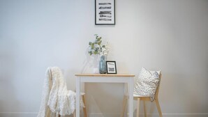 A room with a white table, a chair with a patterned cushion, and a white chair with a white cover. There is a vase with flowers on the table and a framed picture above it. - Walk To Darling Harbour 1 BED NEW APT Nsy188 (Sydney)