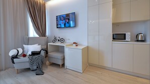 A modern living room with a sofa, a small table, a television, and a kitchen area with a microwave.