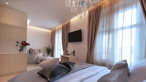 A modern bedroom with a large bed, a TV mounted on the wall, and a chandelier.