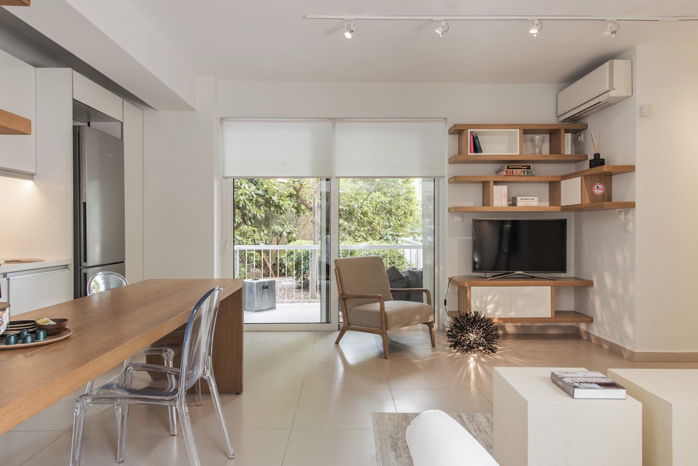 Een moderne keuken met een houten eettafel, transparante stoelen en een ingebouwde televisie.