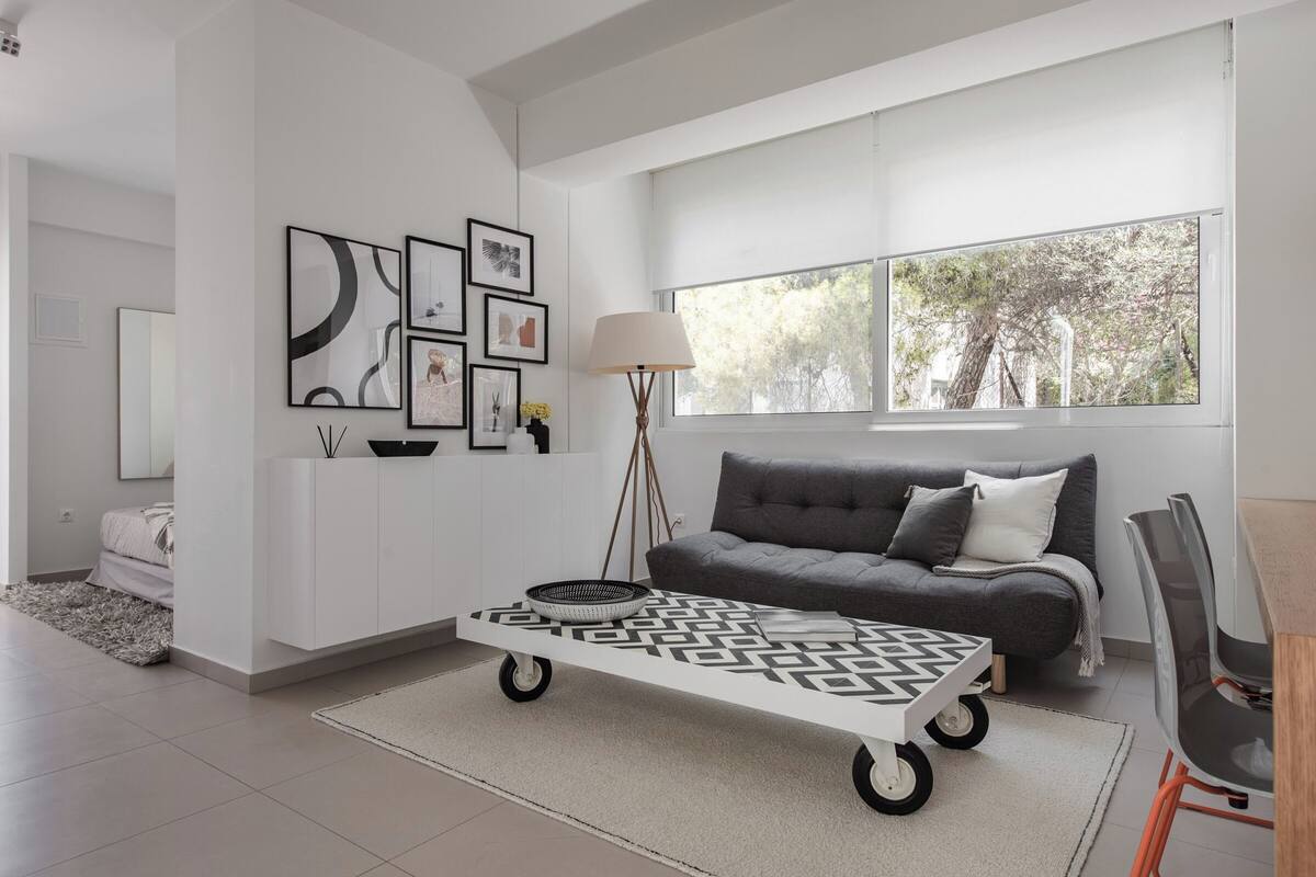 Ein modernes Wohnzimmer mit einem grauen Sofa, einem Couchtisch mit Muster und einem großen Fenster mit Blick auf Bäume.