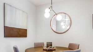 A dining area with a round wooden table, two grey upholstered chairs, a modern pendant light, and a round mirror on the wall. - Picture Perfect (Atlanta)