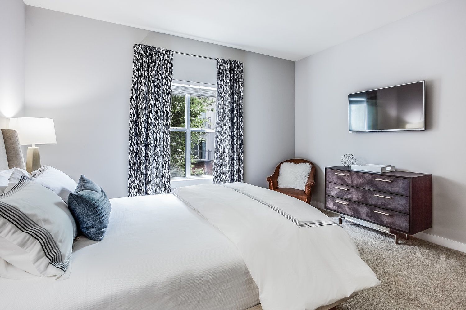 Ein modernes Schlafzimmer mit einem großen Bett, einem Schminktisch, einem Sessel und einem Fernseher.